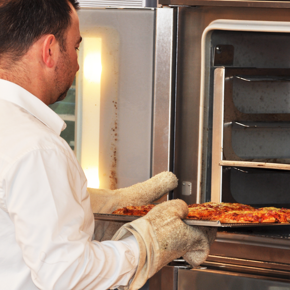 Bäcker nimmt Pizza aus dem Backofen