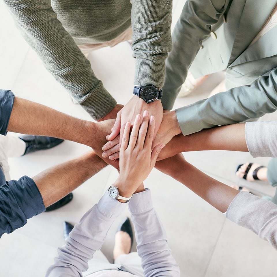 Ein Bild, das die Hände von fünf Personen zeigt, die sich in einem Kreis versammeln und einander berühren, symbolisiert Teamarbeit und Einheit.